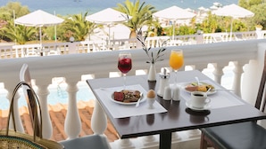 Una mesa de comedor con comida, una copa de vino tinto y un vaso de jugo de naranja, con vista a una piscina y el mar.