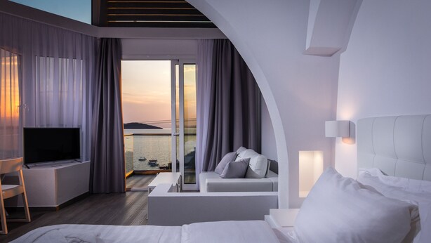 Una habitación de hotel moderna con cama, televisor, sofá y balcón con cortinas.