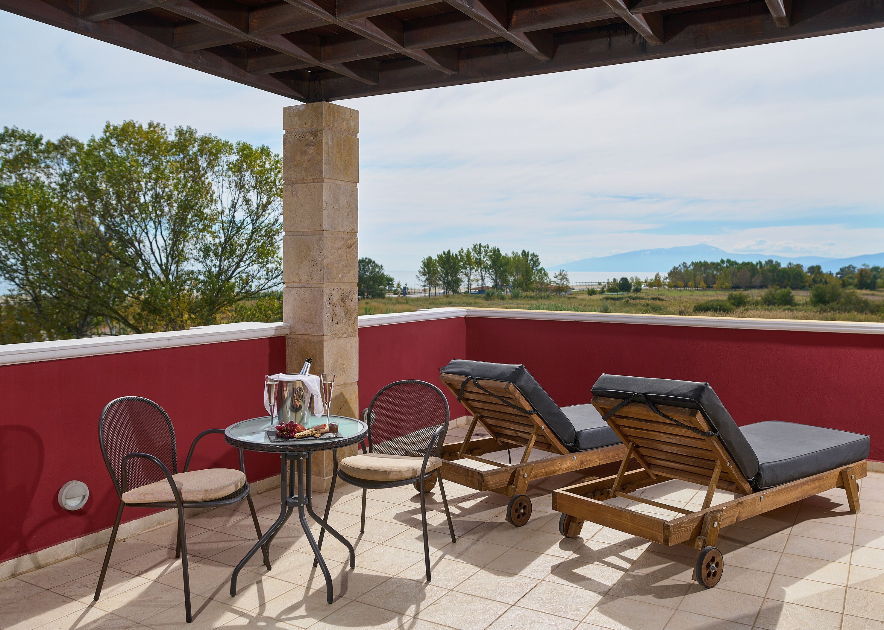 Una terraza con una mesa y sillas, vista del paisaje y un muro rojo.