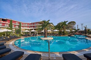 A circular pool with lounge chairs and umbrellas, surrounded by palm trees and a multi-story building with balconies. - Mediterranean Princess - Adults Only (Katerini)
