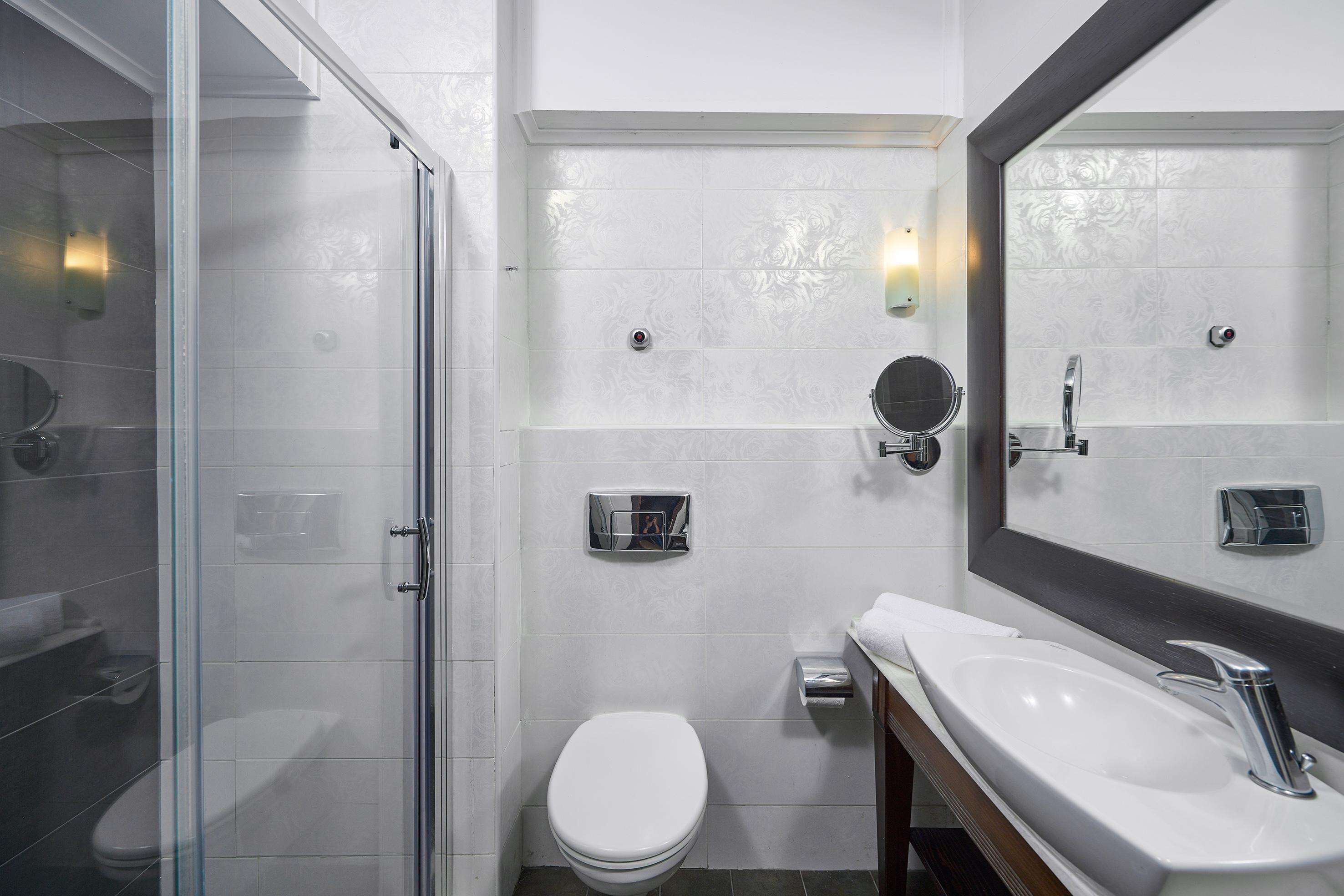 Ein modernes Badezimmer mit Duschkabine aus Glas, Toilette in Weiß, Waschbecken inklusive Spiegel und Handtuchhalter.