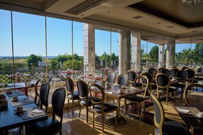 A restaurant with outdoor seating, large windows, and a view of the landscape. - Mediterranean Princess - Adults Only (Katerini)
