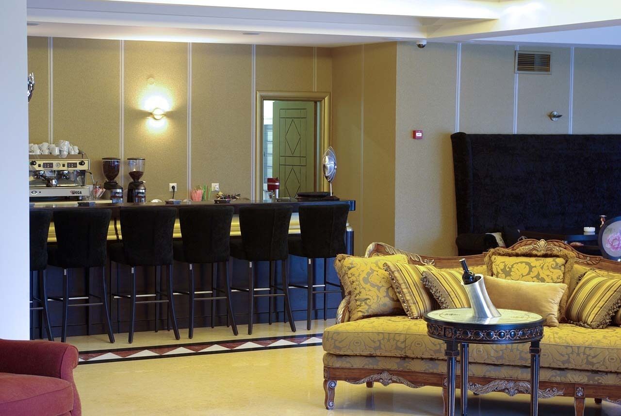 Una zona de bar con una máquina de café, varios taburetes negros y un sofá amarillo con cojines estampados.