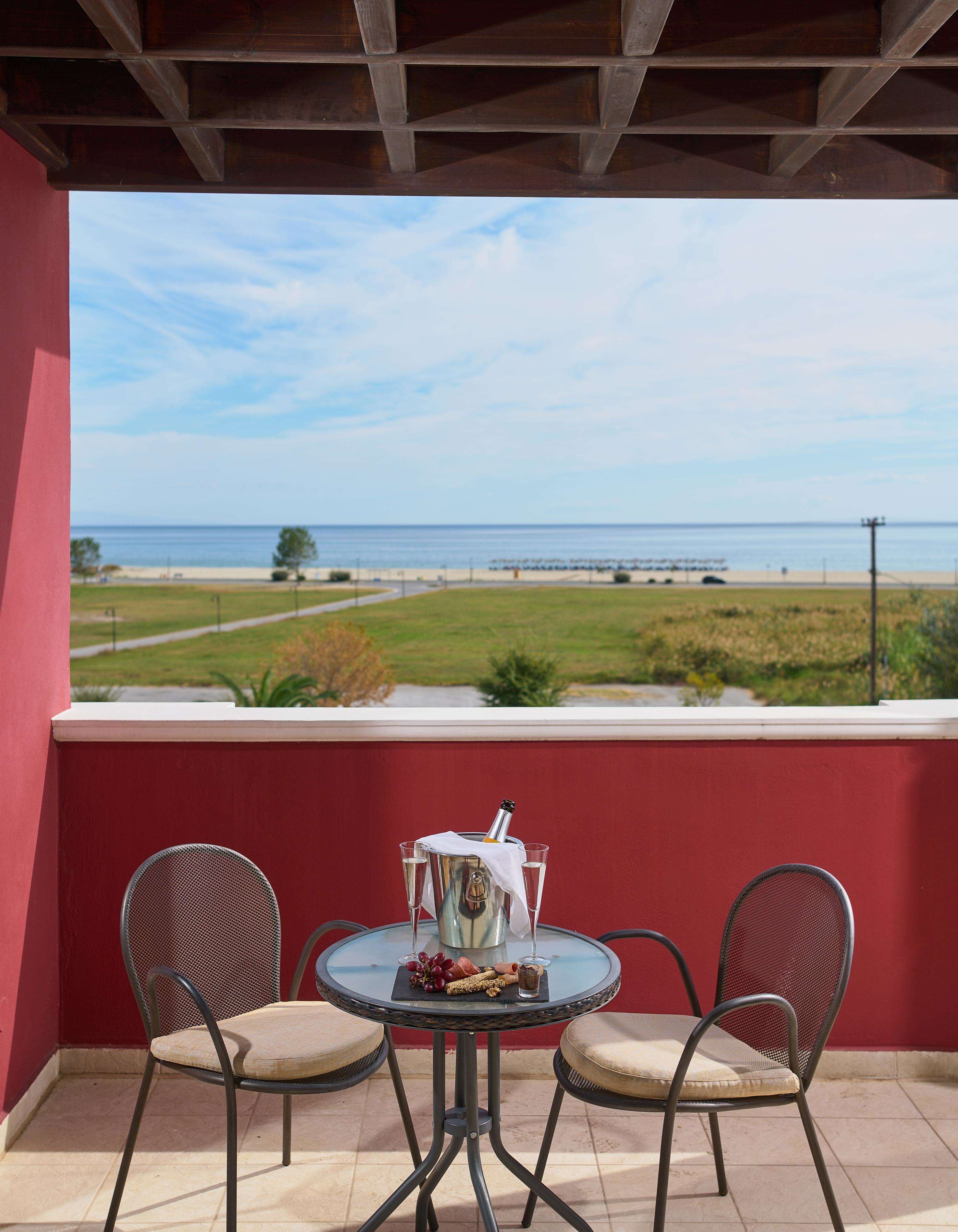 A terrace with a table and two chairs, overlooking a beach and ocean.