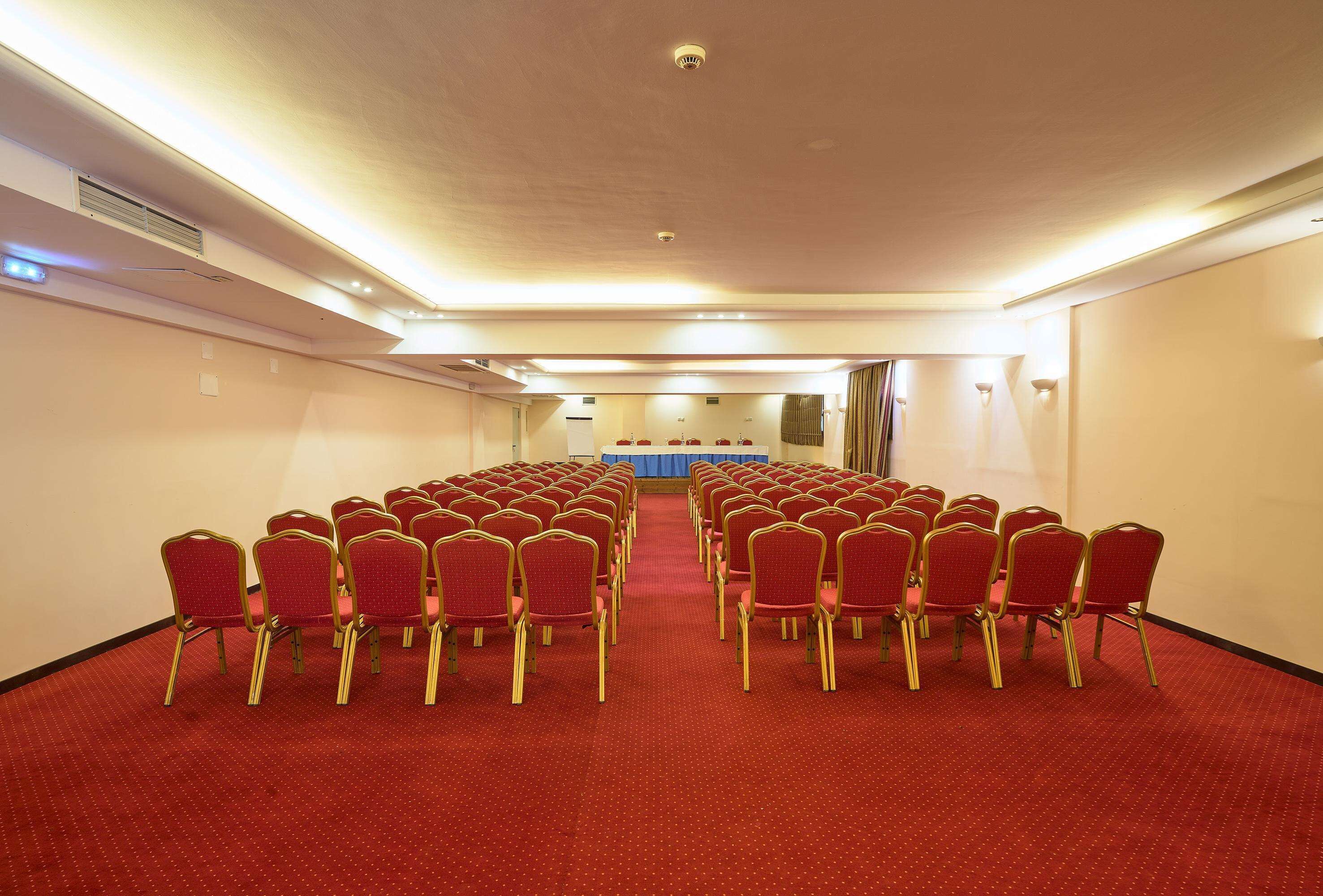 A conference room with rows of red chairs and a blue table at the front.