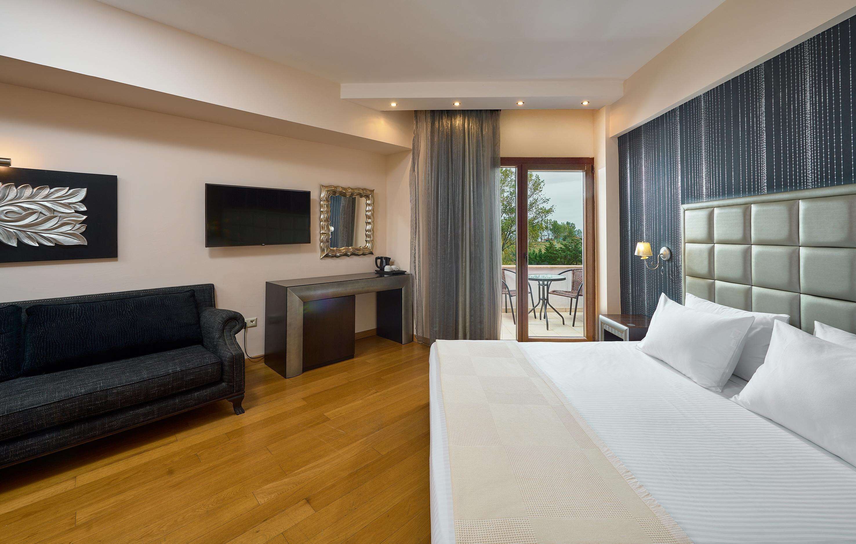 A hotel room with a bed, a desk, a sofa, a TV, and a balcony with a table and chairs.