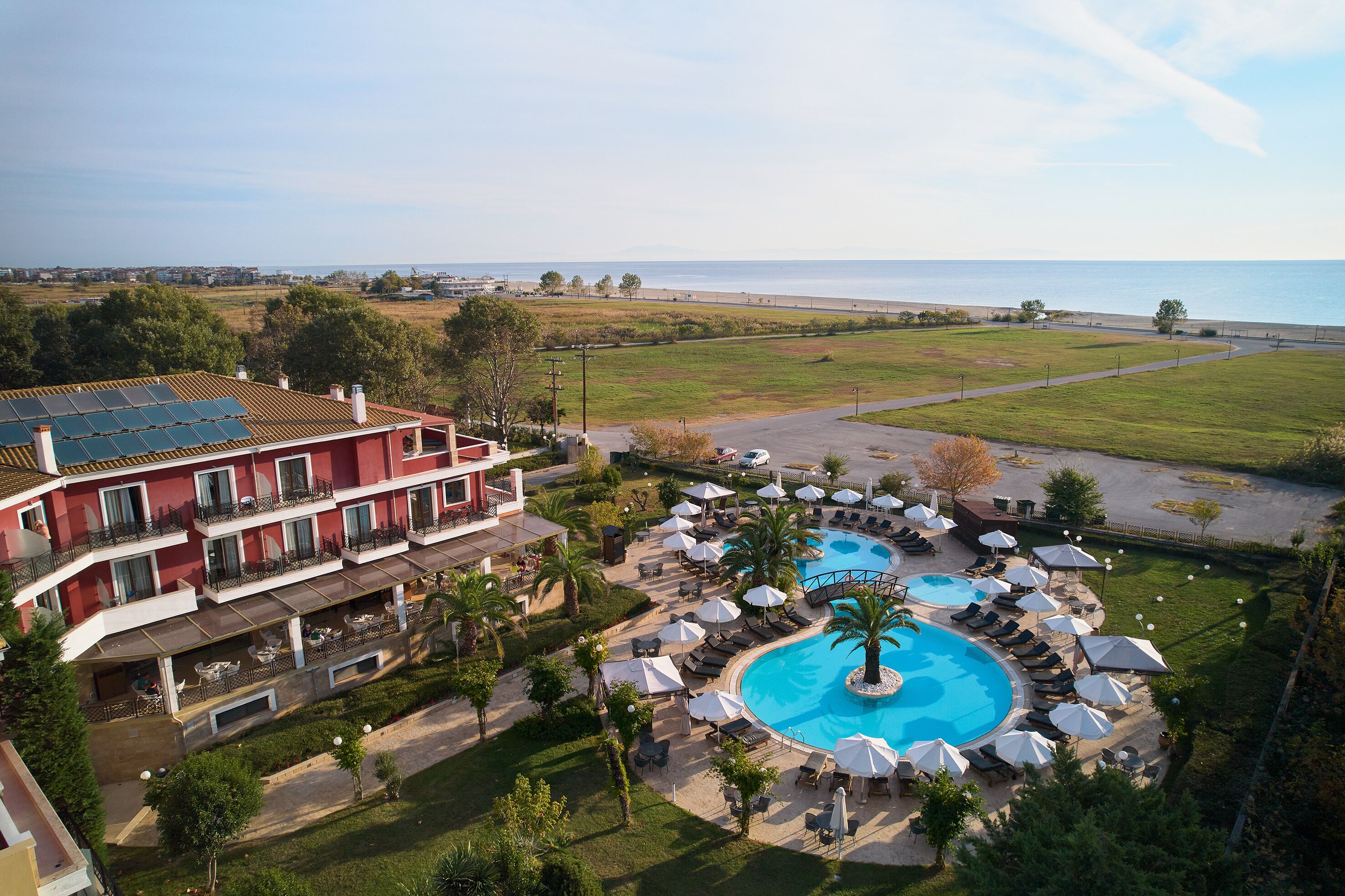 A hotel with a large swimming pool, outdoor seating, and a view of the sea.