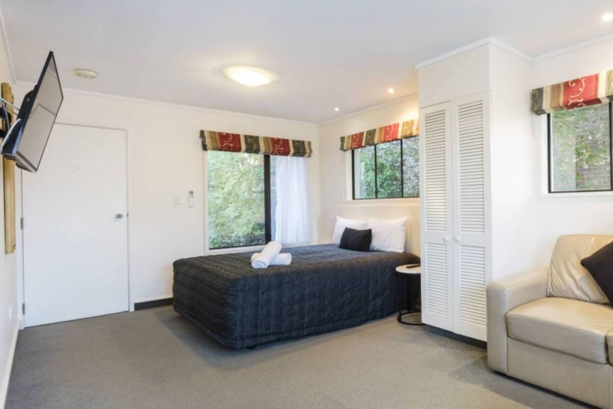 A hotel room with a bed, a sofa, a round table, and a TV mounted on the wall.