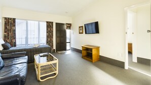 A modern living room with a sofa, a coffee table, a TV, and a door leading to a bathroom. - 755 Regal Court (Dunedin)