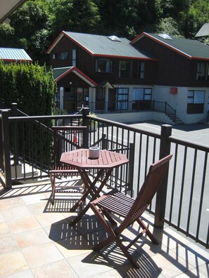 A balcony with a wooden table and chairs, a metal railing, and a view of a building with a red roof and windows. - 755 Regal Court (Dunedin)