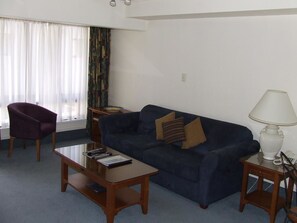 A living room with a dark blue sofa, a wooden coffee table, a purple armchair, and a white lamp on a side table. - 755 Regal Court (Dunedin)