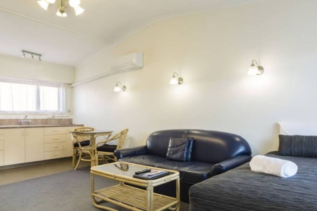 A compact room with a sofa, a small table, a chair, a bed, and a kitchenette.