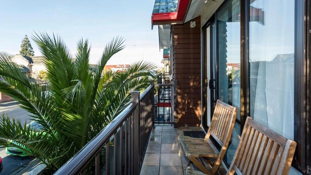 A balcony with wooden benches, a railing, and a view of palm trees and buildings. - 755 Regal Court (Dunedin)