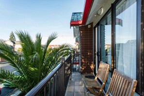A balcony with wooden benches, a railing, and a view of palm trees and buildings. - 755 Regal Court (Dunedin)
