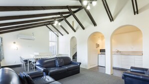 A spacious living area with a black leather sofa, a dining table with chairs, and a kitchen in the background. - 755 Regal Court (Dunedin)