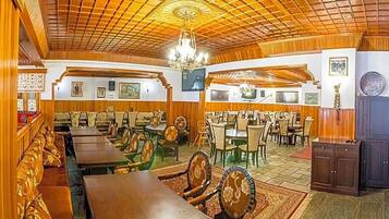 Un restaurante con techo y paredes de madera, varias mesas y sillas para comer, y una araña.