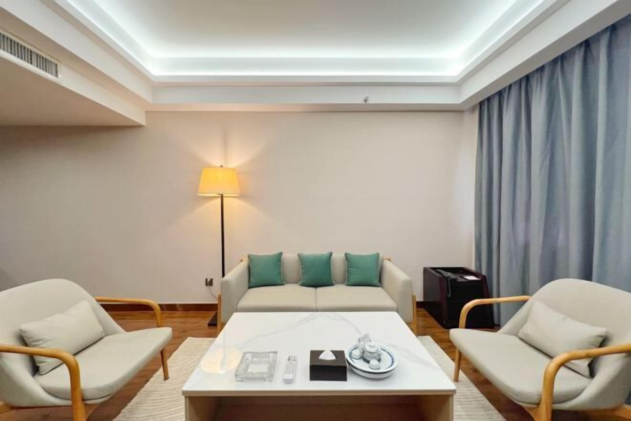 Une chambre d’hôtel moderne équipée d’un canapé, de deux fauteuils, d’une table basse et d’une lampe.