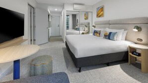 Ett modernt hotellrum med en stor säng, en platt-TV, ett nattduksbord och en liten lampa.