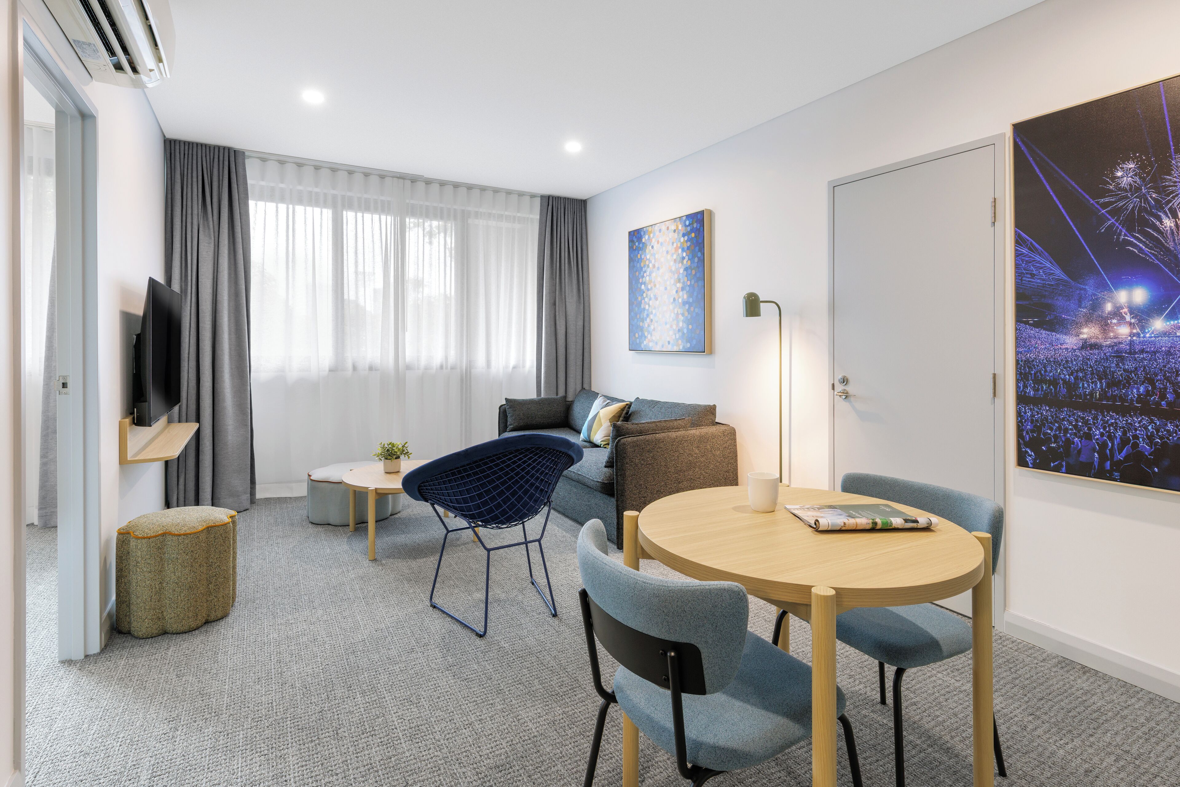 A modern hotel room with a sofa, a round table, a television, and a large window with curtains.