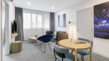 Una habitación de hotel moderna con un sofá, una mesa redonda, un televisor y un ventanal con cortinas.