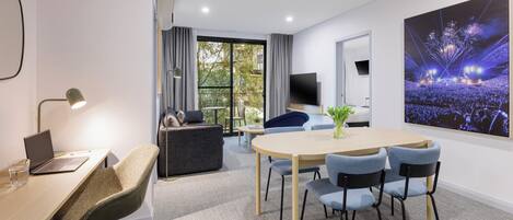 A modern office space with a round table, chairs, a laptop, and a TV on the wall.