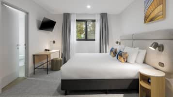 A modern hotel room with a large bed, a desk, a flat-screen TV, and a view of the outdoors.