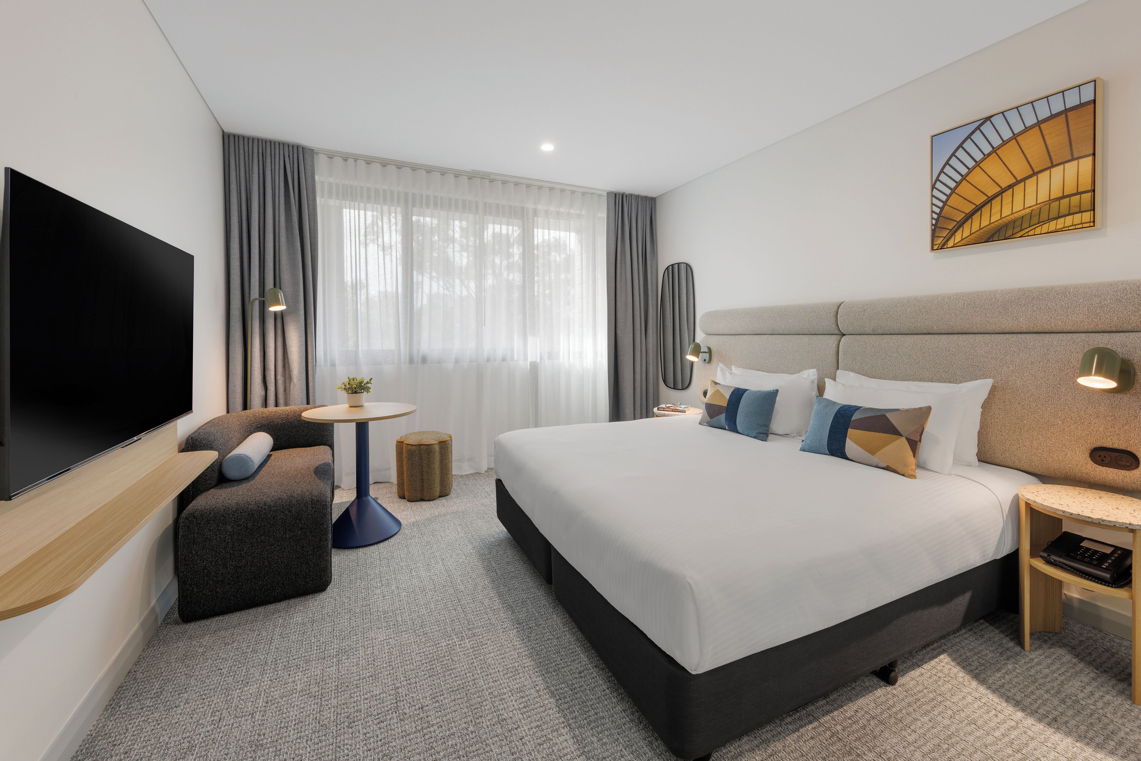Een moderne hotelkamer met een groot bed, een flatscreen televisie, een bank, een kleine tafel en een schilderij aan de muur.