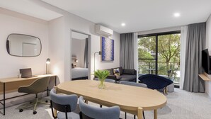 Ett modernt hotellrum med en matplats, en soffa, en TV och ett stort fönster.