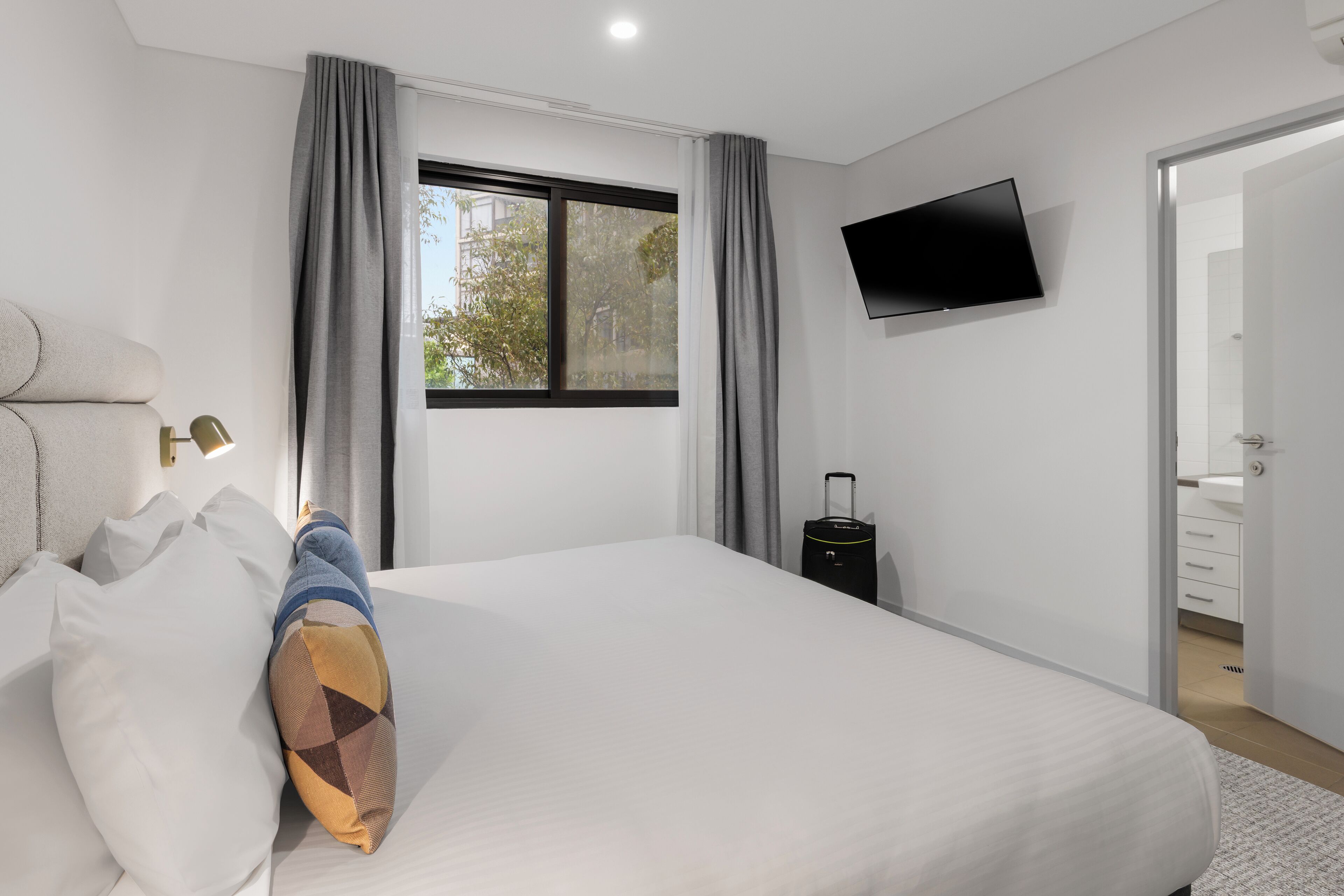 Una habitación de hotel moderna con una cama grande, un televisor de pantalla plana en la pared y una maleta en el suelo.