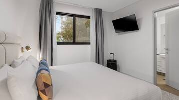 Una habitación de hotel moderna con una cama grande, un televisor de pantalla plana en la pared y una maleta en el suelo.