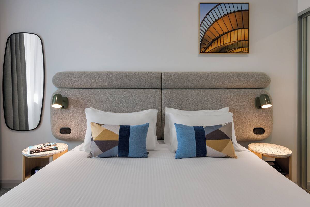 A hotel room with a large bed, two bedside tables, a mirror, and a painting on the wall.
