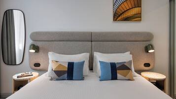 A hotel room with a large bed, two bedside tables, a mirror, and a painting on the wall.