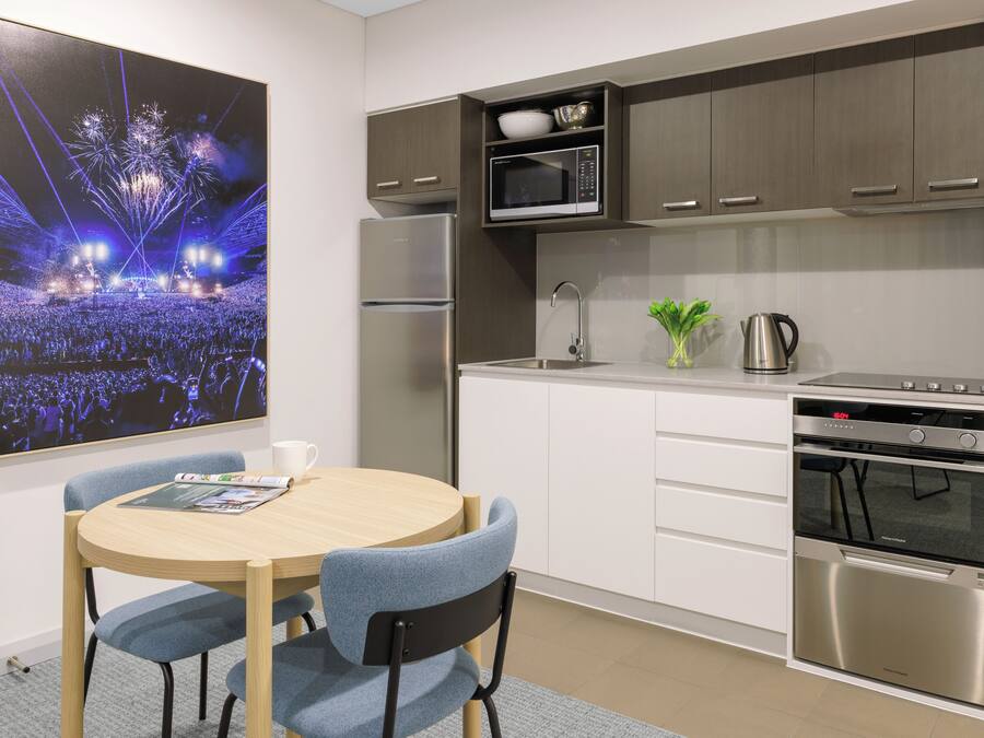 A modern kitchen with a built-in microwave, oven, and refrigerator. There is a dining table with chairs and a framed picture on the wall.