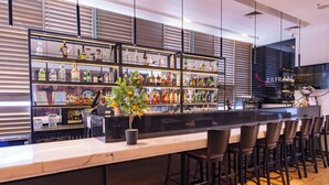 A bar area with a long counter, multiple shelves of bottles, and several bar stools. - Wyndham Concepcion Pettra (Hualpén)