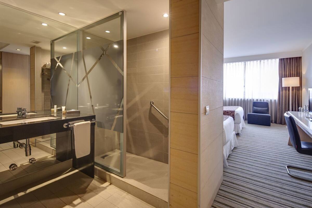 A hotel bathroom with a glass shower enclosure, a sink with a mirror, and a toilet.