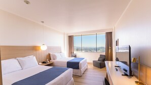 A hotel room with two beds, a desk with a TV, and a large window with a city view. - Wyndham Concepcion Pettra (Hualpén)