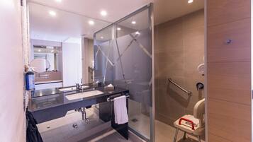 A modern bathroom with a glass shower enclosure, a vanity with two sinks, and a wheelchair-accessible toilet.