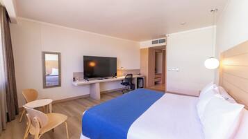 Una habitación de hotel con una cama, un escritorio con televisor, una silla y un espejo.