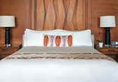 A neatly made bed with a white duvet and decorative pillows, flanked by wooden nightstands with lamps and a radio.