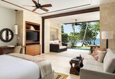 A spacious bedroom with a large bed, a desk, a television, and a balcony with a view of the ocean.