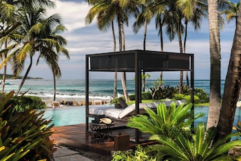 A beachside dining setup with a table, chairs, and candles, overlooking the ocean and palm trees. at Dorado Beach, a Ritz-Carlton Reserve