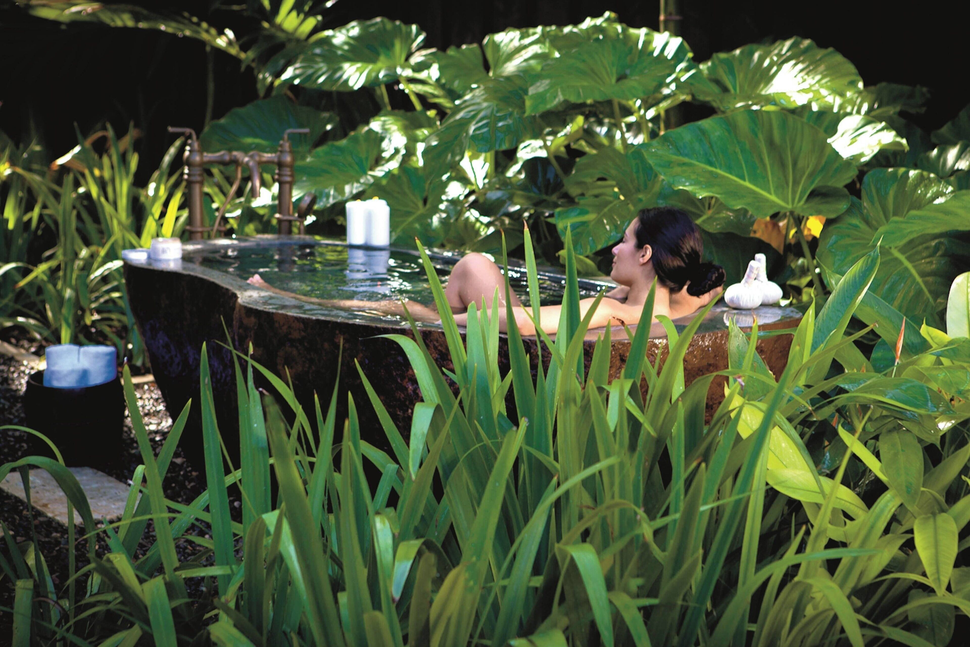 A person relaxing in a hot tub surrounded by lush greenery.