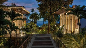 A modern building with a wooden deck and palm trees, overlooking a body of water.