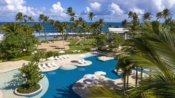 Een resort met een groot zwembad, palmbomen en uitzicht op de oceaan.
