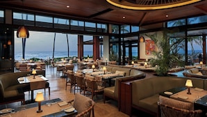 A spacious restaurant with high ceilings, large windows, and a view of the ocean.