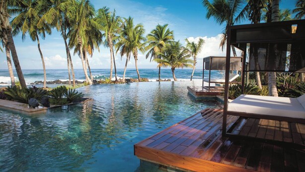 A poolside area with wooden deck, lounge chairs, and palm trees.