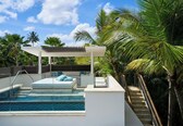 A modern outdoor pool area with a pergola, a seating area with cushions, and a staircase leading down to the pool.