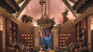 A grand hall with a marble table, hanging plants, and wall-mounted lanterns.
