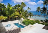 A poolside area with a clear view of the beach and ocean, surrounded by palm trees.