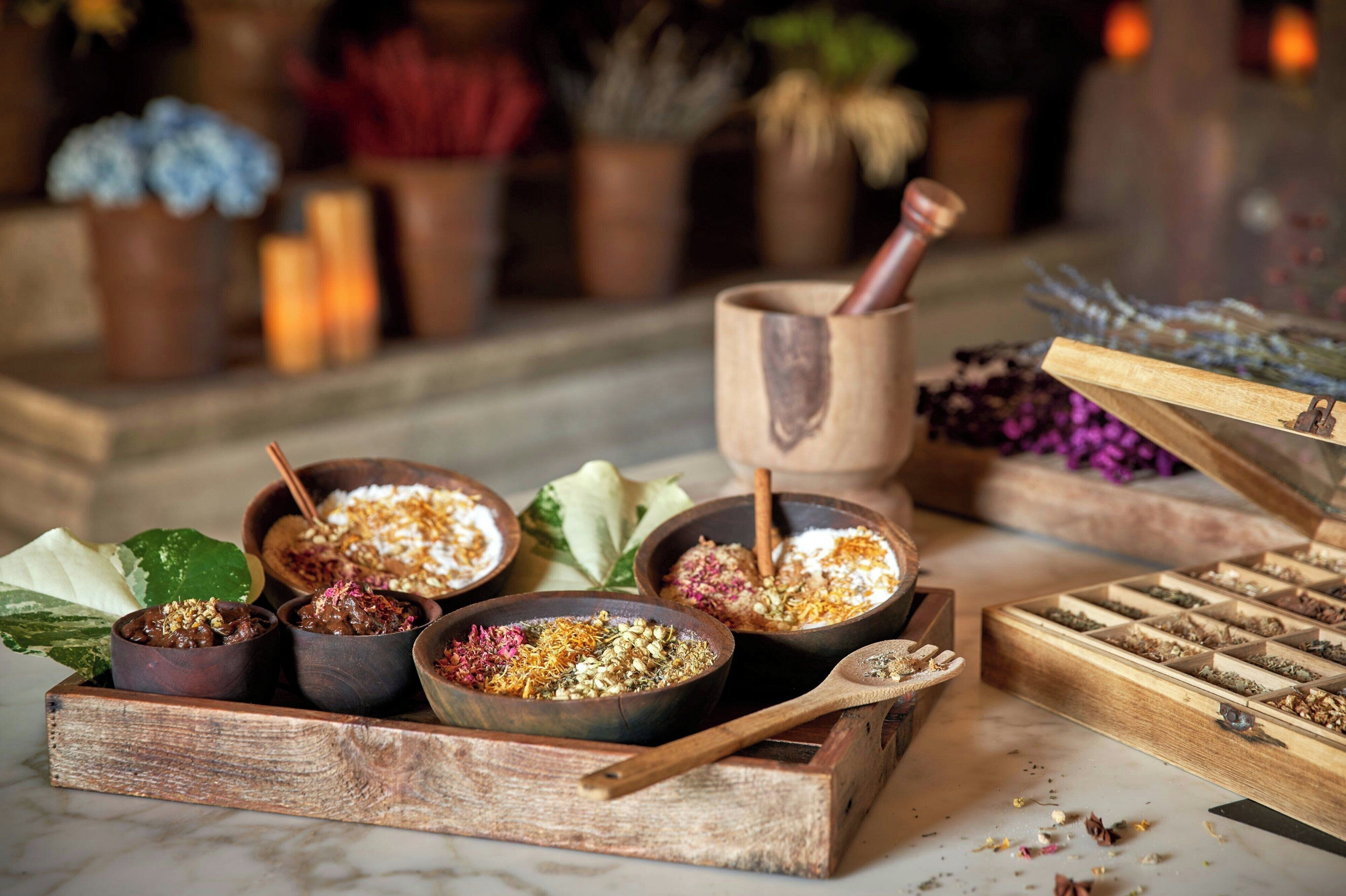 A wooden tray with bowls containing various food items and a wooden box with compartments of dried herbs.